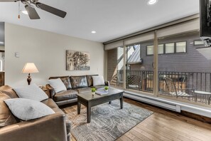 Un salon moderne avec un canapé en cuir, une table basse et une grande fenêtre donnant sur un balcon.