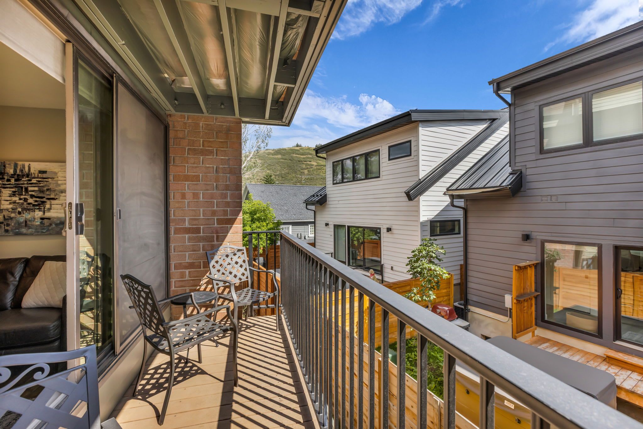 A balcony with a seating area, a view of neighboring houses, and a clear sky.