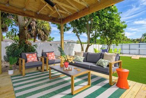 An outdoor patio with a wooden deck, a gray sofa set, and a striped rug. - Backyard Paradise • Grill • Game Room • Putt Putt (Palm Springs)