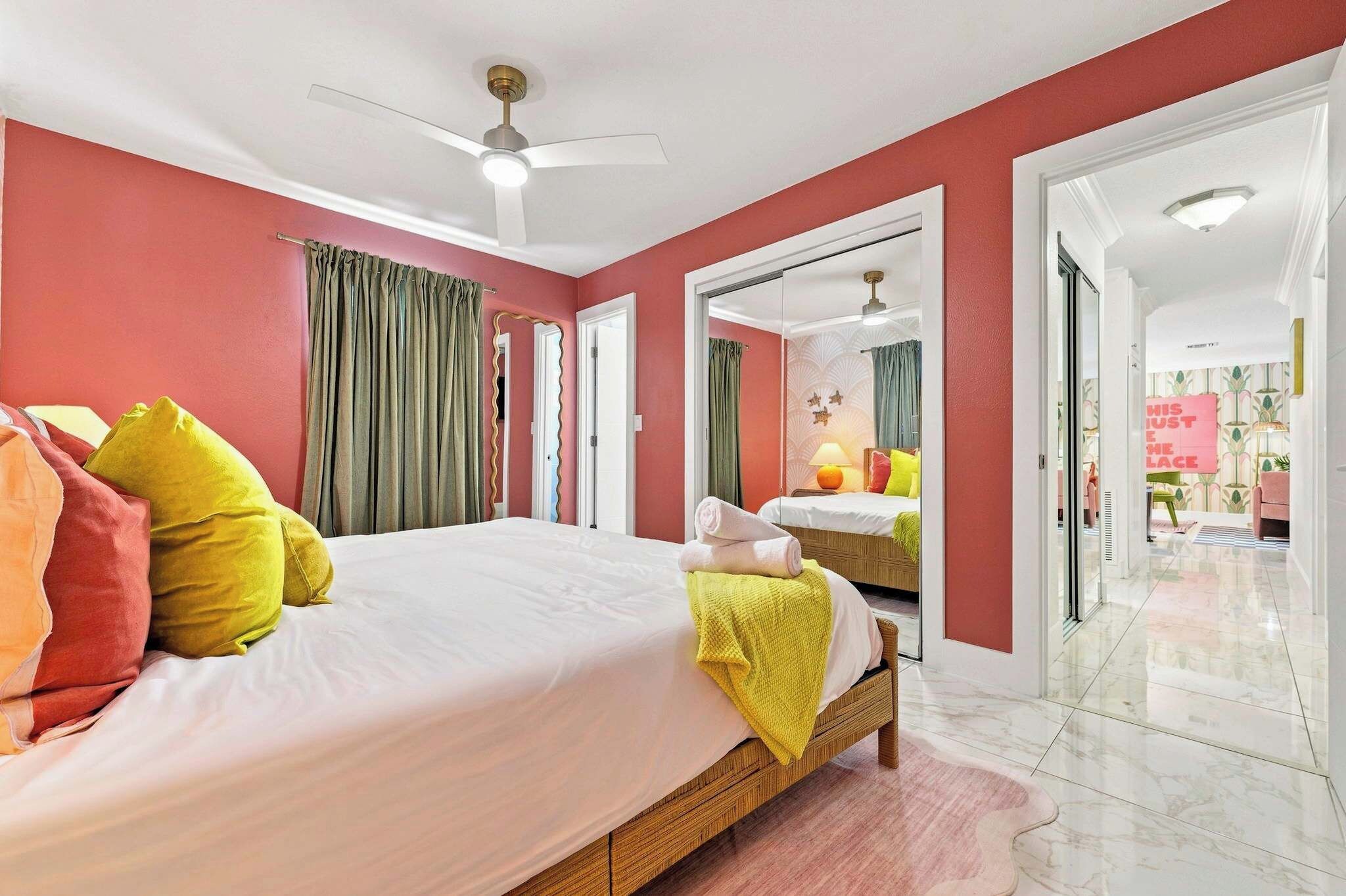 A hotel room with a large bed, a ceiling fan, and a view into the adjacent room.
