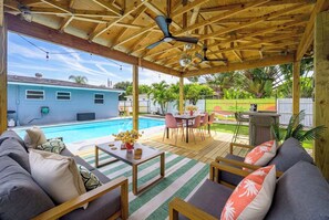 A covered outdoor seating area with a pool, a dining table, and a sofa. - Backyard Paradise • Grill • Game Room • Putt Putt (Palm Springs)