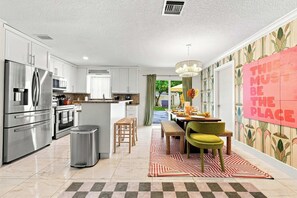 A modern kitchen with stainless steel appliances, a dining area with a patterned rug, and a bold statement wall. - Backyard Paradise • Grill • Game Room • Putt Putt (Palm Springs)