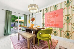 A dining area with a table set for four, a bench, a green chair, and a decorative wall piece. - Backyard Paradise • Grill • Game Room • Putt Putt (Palm Springs)