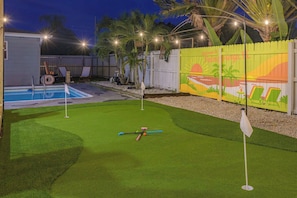Ein Garten mit Pool, Kunstrasen, einer Golf-Putting-Fläche und einem Zierzaun.
