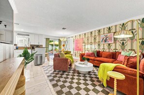 A modern living room with a checkered floor, a red sofa, a pink armchair, and a dining area with a yellow umbrella. - Backyard Paradise • Grill • Game Room • Putt Putt (Palm Springs)