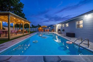 A swimming pool with a covered patio area, a barbecue grill, and a house in the background. - Backyard Paradise • Grill • Game Room • Putt Putt (Palm Springs)