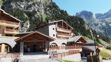 Un chalet de montagne à plusieurs étages, construit en pierre et en bois, doté de balcons et offrant une vue sur les montagnes environnantes.