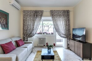 A living room with a sofa, a coffee table, a TV, and a window with curtains. - 2-Bedroom Apartment with a Balcony, a 10-Minute Walk from Vatican City (Roma)