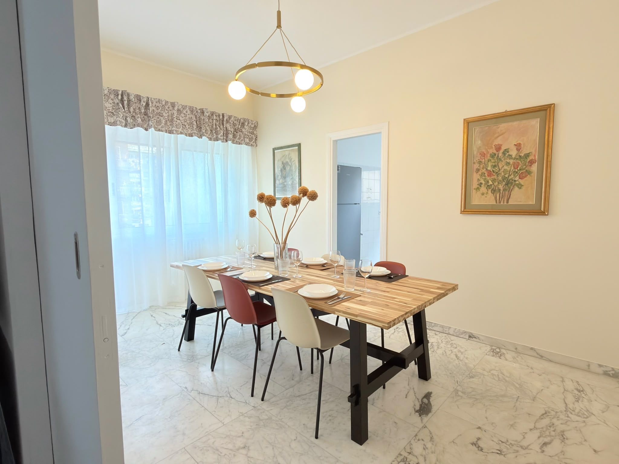 A dining area with a wooden table set for four, surrounded by chairs, a chandelier, and a painting on the wall.