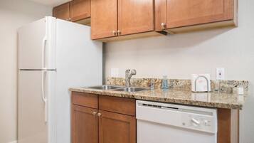 A kitchen with wooden cabinets, a white refrigerator, a granite countertop, a stainless steel sink, and a dishwasher.