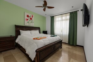 Ein Schlafzimmer mit Bett, Nachttisch, Kommode, Deckenventilator, einem Gemälde und einem Fernseher.