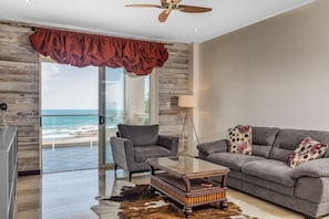 A modern living room with a view of the ocean, a ceiling fan, a glass coffee table, and a leather sofa with decorative pillows. - Luxury Oceanfront 2-bedroom condo in enchanting Jacó on the Beach!!! (Jacó)