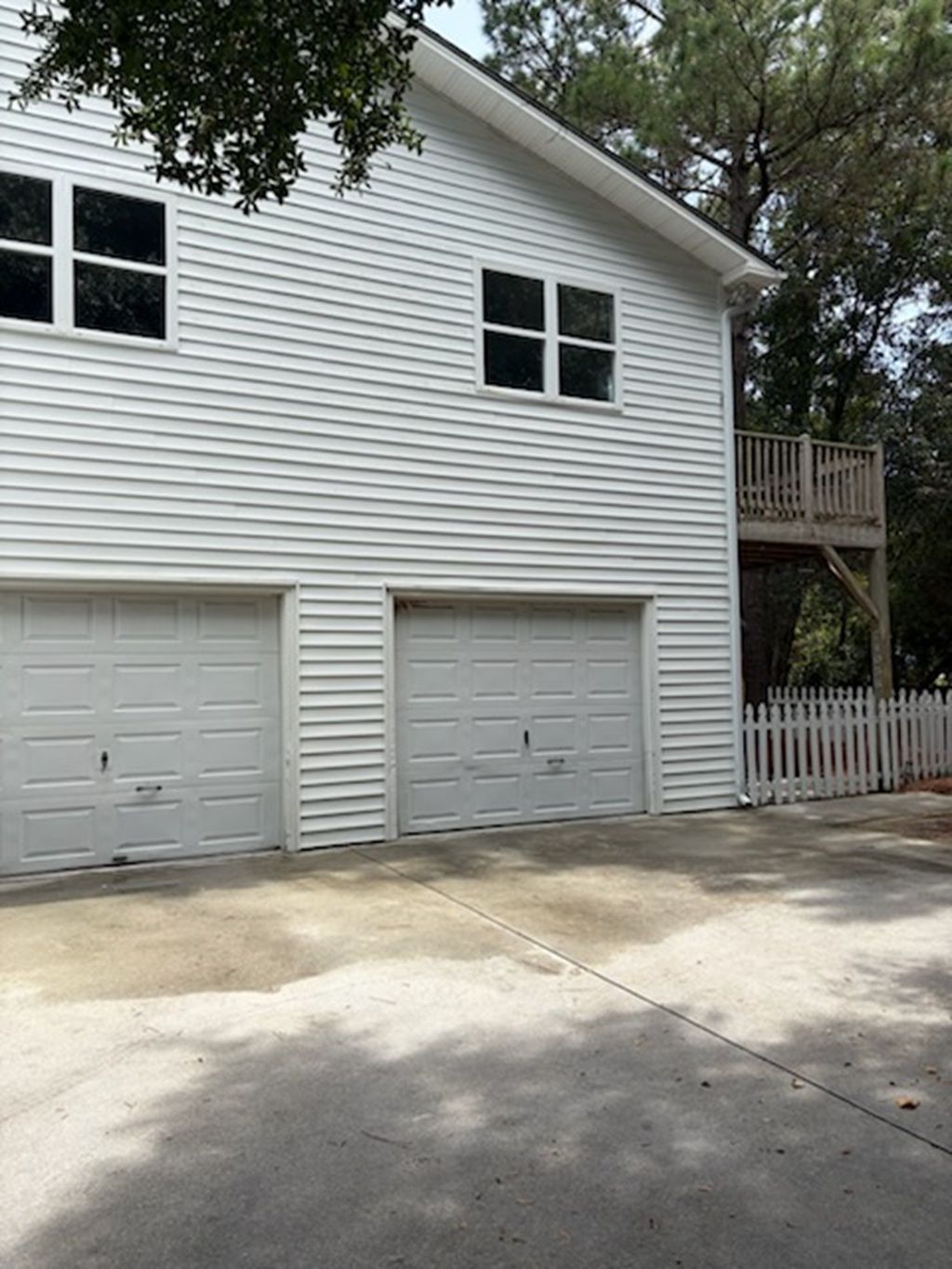 A two-story building with a white exterior, two garage doors, and a wooden deck with a white picket fence.