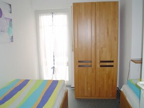A bedroom with a wooden wardrobe, a bed with a striped bedspread, and a bedside table with a lamp. - Park Residence Am Hafen 32 (Zingst)