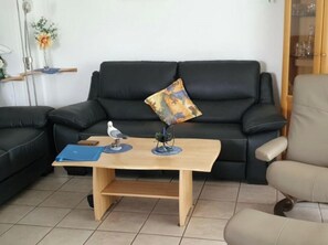 A living room with a black leather sofa, a wooden coffee table, and a beige armchair. - Park Residence Am Hafen 32 (Zingst)