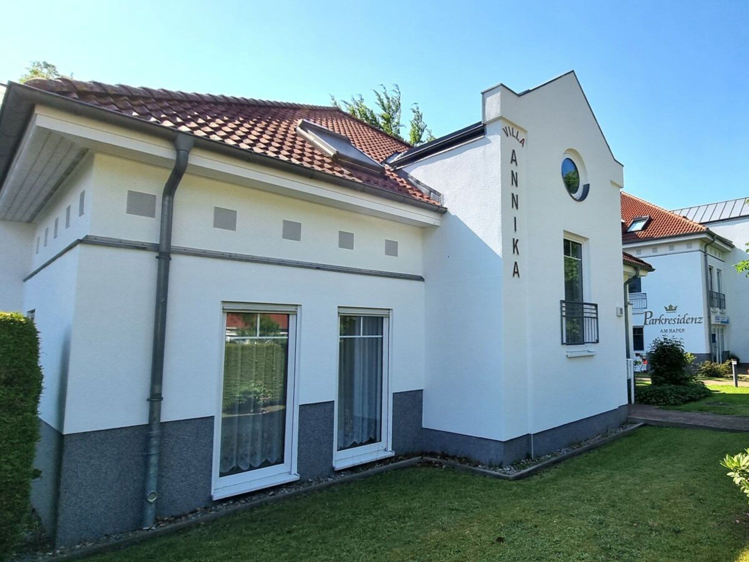 Ein modernes Gebäude mit heller Fassade, einem roten Ziegeldach und einem Schild, auf dem 'Villa Anika' steht.