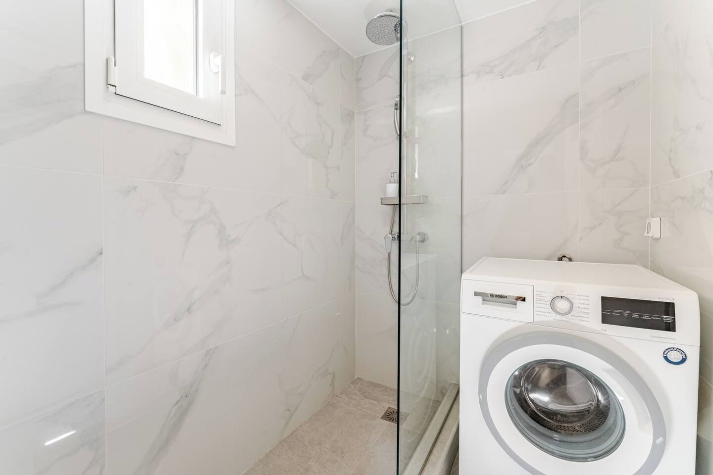 Een badkamer met een douchecabine van glas, een Bosch wasmachine en wanden met een marmerlook.