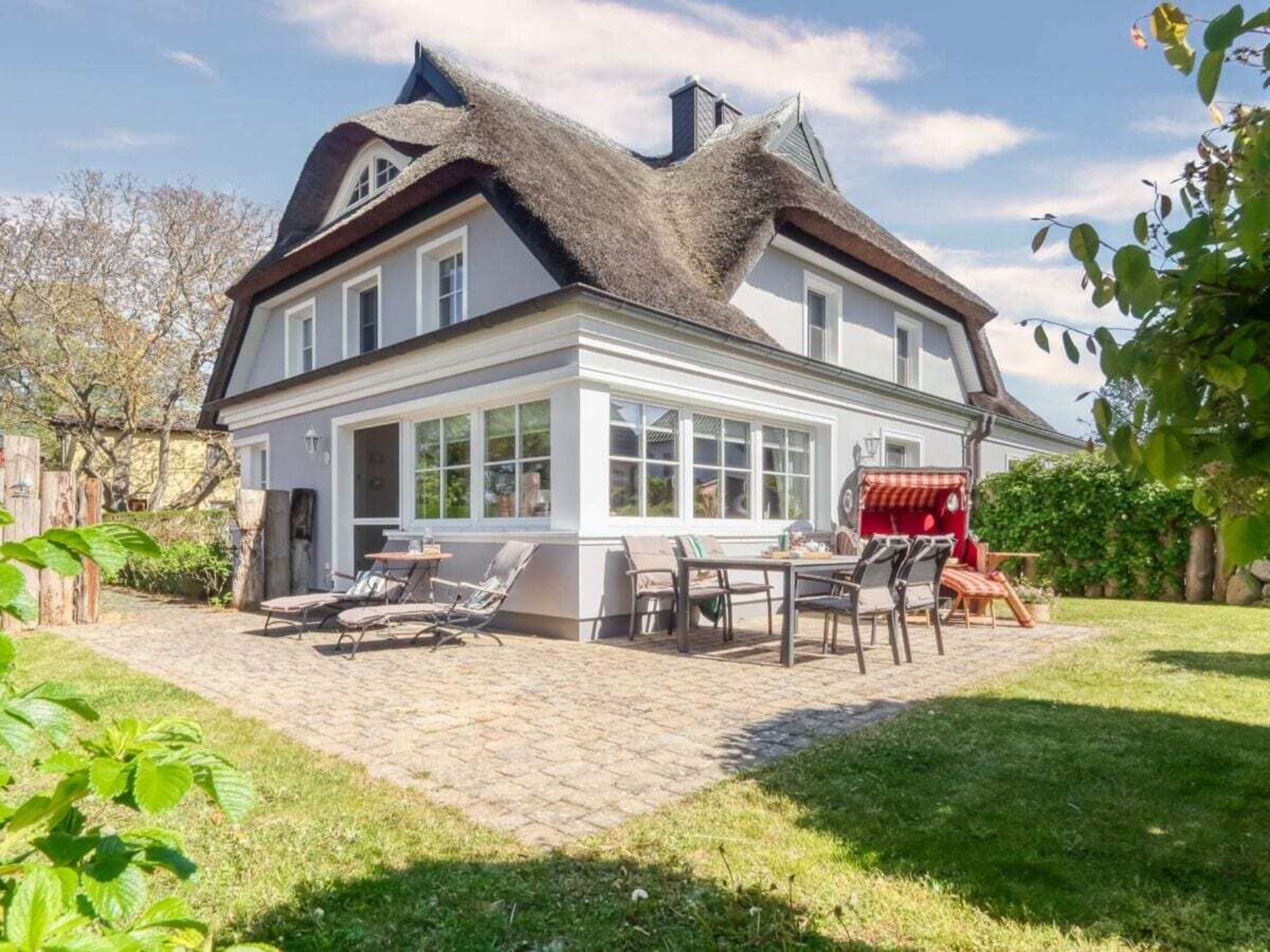 A two-story house with a thatched roof, a patio with outdoor furniture, and a large windowed front area.