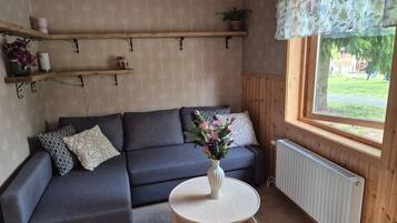 Una habitación acogedora con un sofá seccional gris, una mesita redonda con un jarrón de flores y una ventana con vistas a la vegetación.