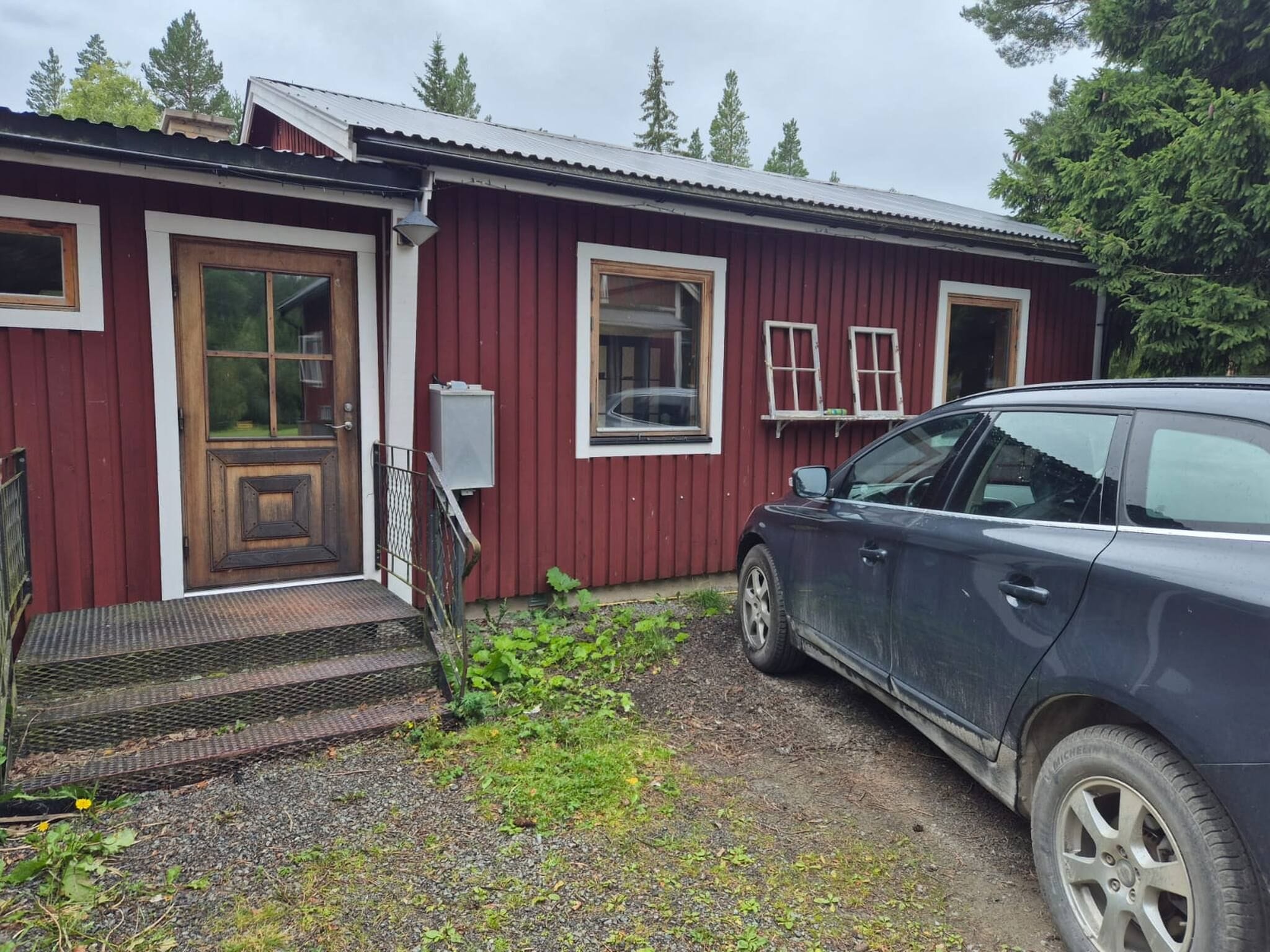 Ett rött trähus med en ytterdörr, en liten veranda och en bil parkerad framför.