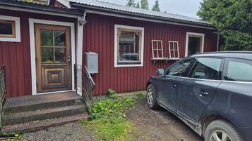 Ett rött trähus med en ytterdörr, en liten veranda och en bil parkerad framför.