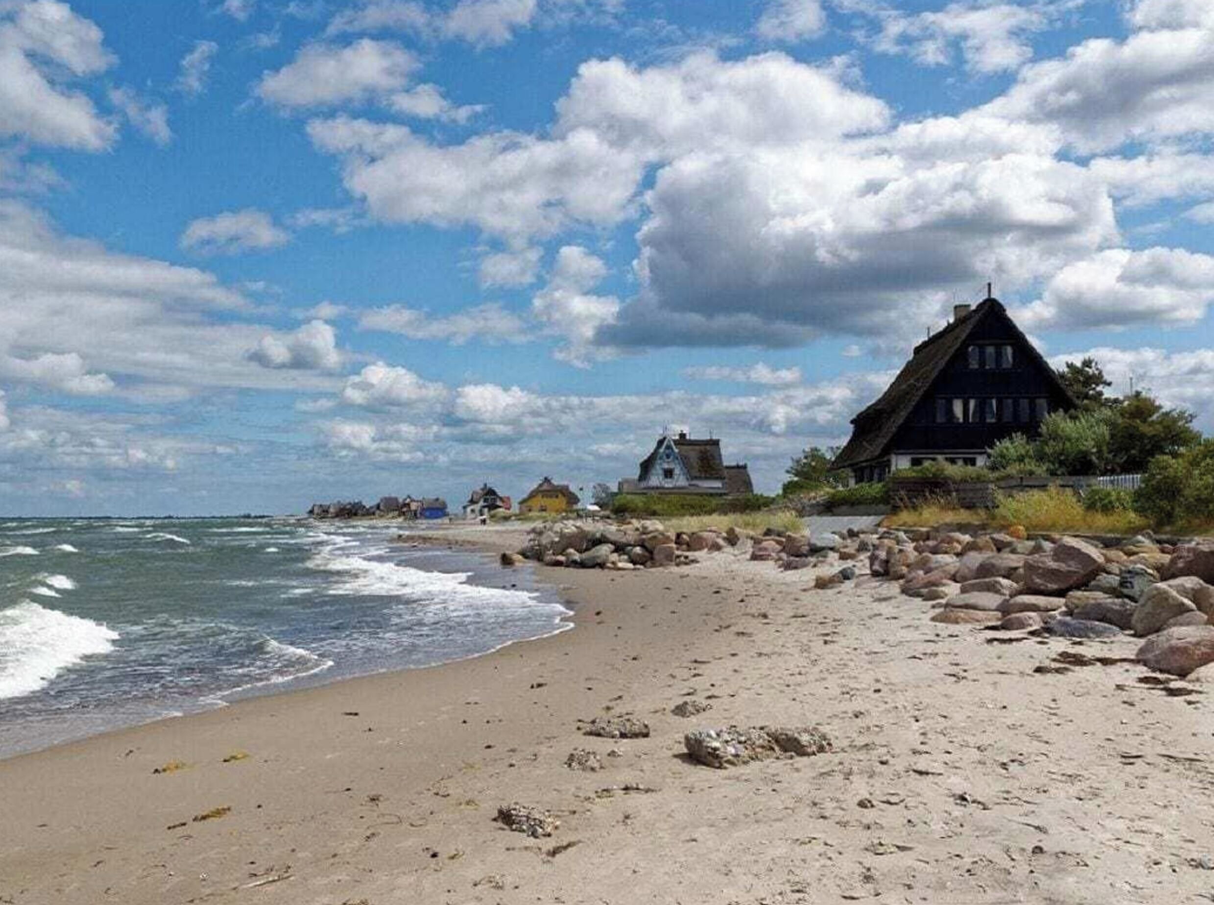 A beach with a row of traditional houses, a rocky shoreline, and a clear sky.
