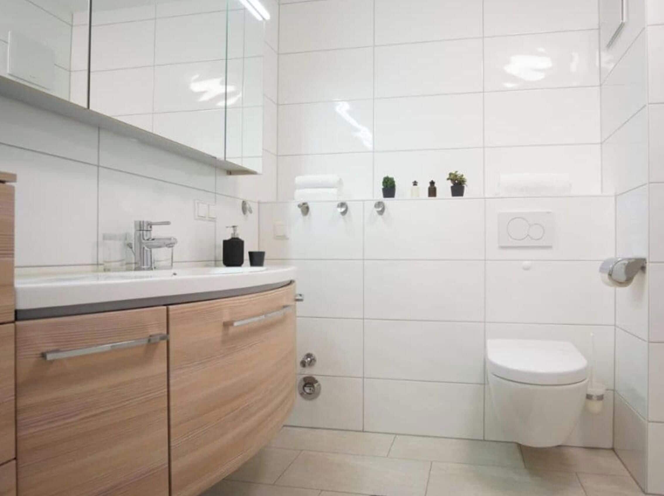 Une salle de bain moderne avec des toilettes blanches, un lavabo avec un miroir et un meuble avec des tiroirs.