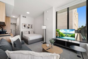 Ein modernes Hotelzimmer mit Bett, Sofa, Fernseher und einem Balkon mit Blick auf die Stadt.