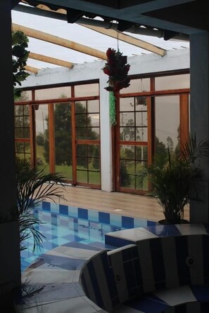 Ett takförsett utomhusområde med en pool, krukväxter och en pergola.