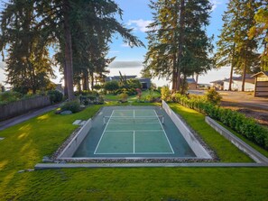 A tennis court surrounded by trees and a building in the background. - The Heron at Black Pearl | Dyes Inlet Retreat (Bremerton)