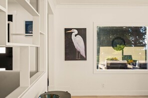 Ein Zimmer mit einem großen Fenster, einem Vogelgemälde und Blick auf einen Baum.