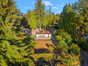 Una propiedad residencial rodeada de un bosque frondoso, con una casa central, una terraza visible y un césped bien cuidado.