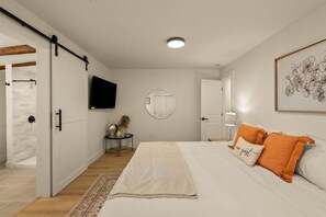 Ein Schlafzimmer mit einem großen Bett, einem Fernseher, einem runden Spiegel und einer Tür zu einem weiteren Raum.