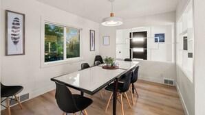 Et moderne spiseområde med et glasbord, sorte stole og en hængende lampe.