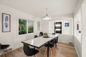 Un área de comedor moderna con una mesa de vidrio, sillas negras y una lámpara colgante.