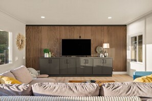 A modern living room with a large flat-screen TV, a dark grey entertainment unit, and a beige sofa. - The Heron at Black Pearl | Dyes Inlet Retreat (Bremerton)