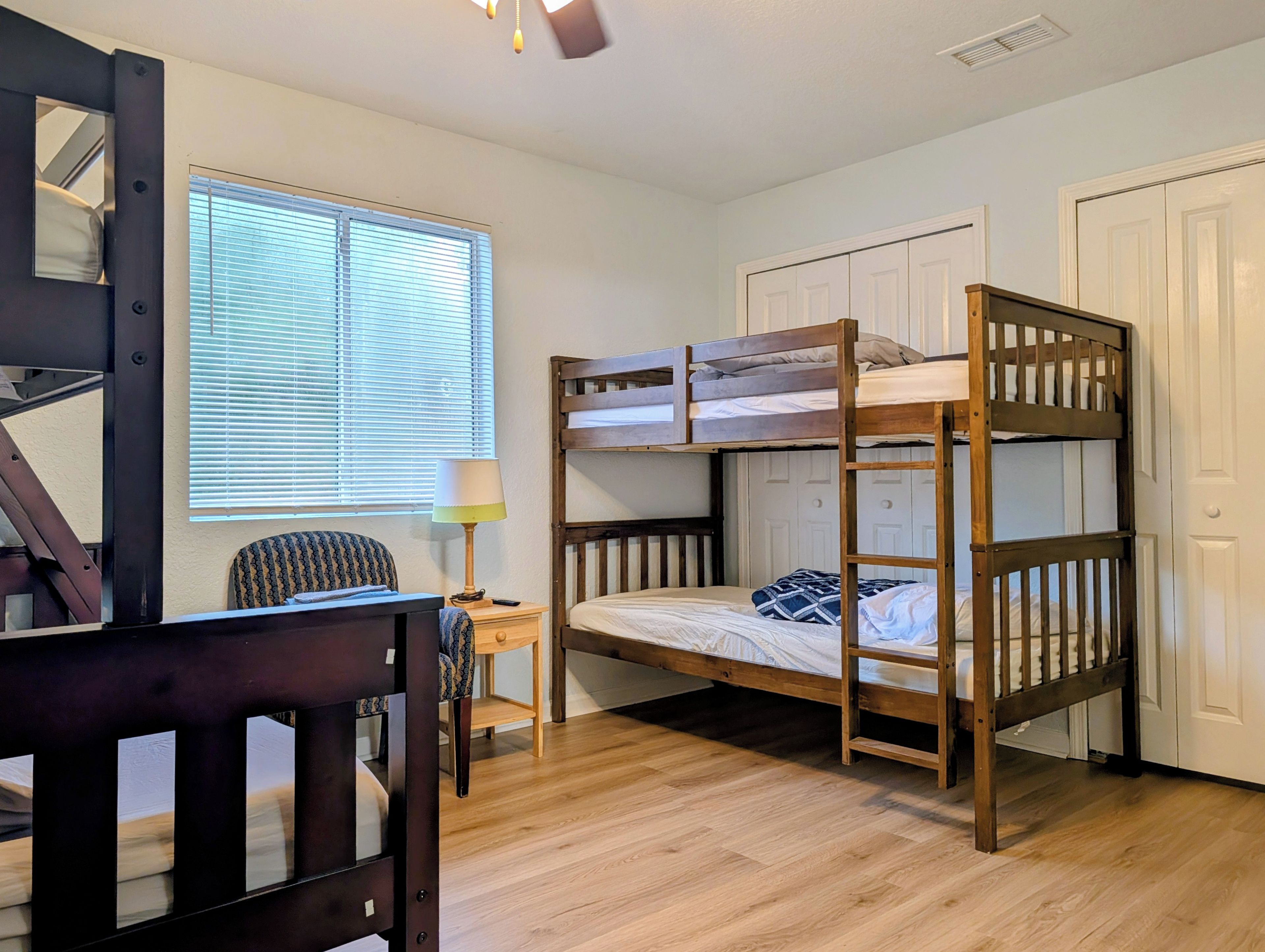 Une chambre avec un lit superposé, un bureau et une chaise, une fenêtre avec des stores et une porte.