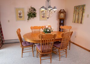 Comedor con mesa y sillas de madera, una araña, un reloj de pared y obras de arte enmarcadas.