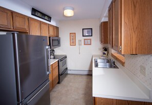 A compact kitchen with wooden cabinets, a stainless steel refrigerator, a microwave, and a sink. - 1BR Ski-in/Ski-out | Free Spring House Pool Access (Ludlow)