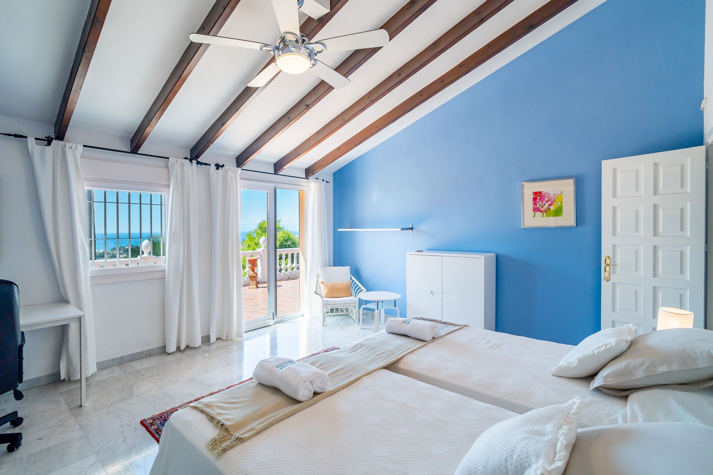 Quarto de hotel com cama, escrivaninha, cadeira, guarda-roupa e vista para o exterior.