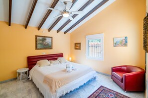 A hotel room with a bed, a red chair, a ceiling fan, and artwork on the walls. - Cubo's Villa Mirador del Mar Family / Private pool / Air conditioning / Sea views / Free Wi-Fi (Vélez Málaga)