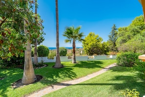 Ein gepflegter Garten mit verschiedenen Bäumen, einem deutlichen Weg und Blick auf das Meer.
