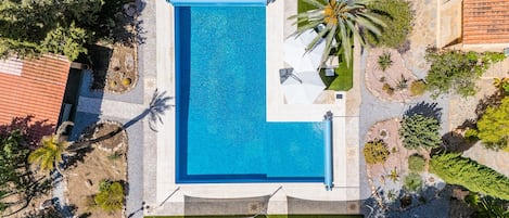 An aerial view of a swimming pool surrounded by greenery and a stone wall.