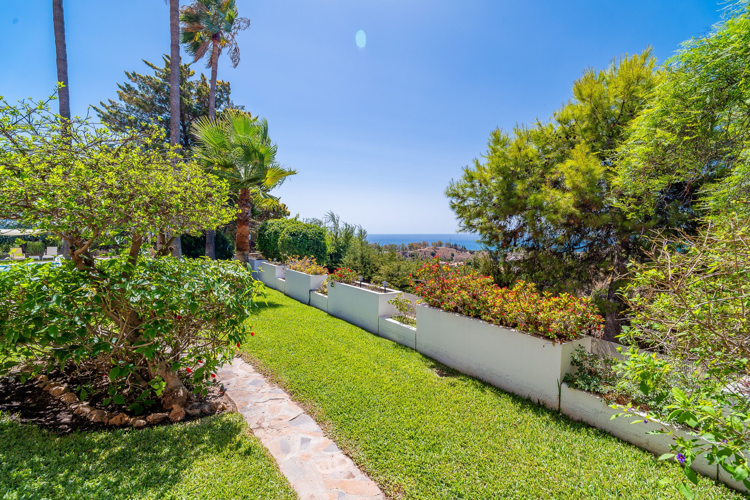 A landscaped garden with a stone pathway leading to a view of the sea.