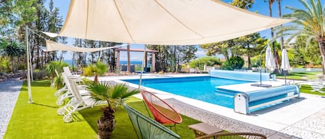 A poolside area with a large canopy, lounge chairs, and a view of the sea.