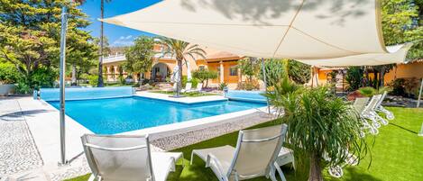A swimming pool with a sunshade, two lounge chairs, and a well-maintained lawn.