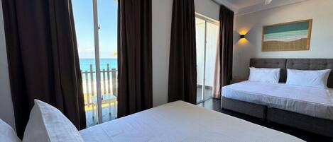 A hotel room with a bed, a ceiling fan, and a view of the sea through large windows.
