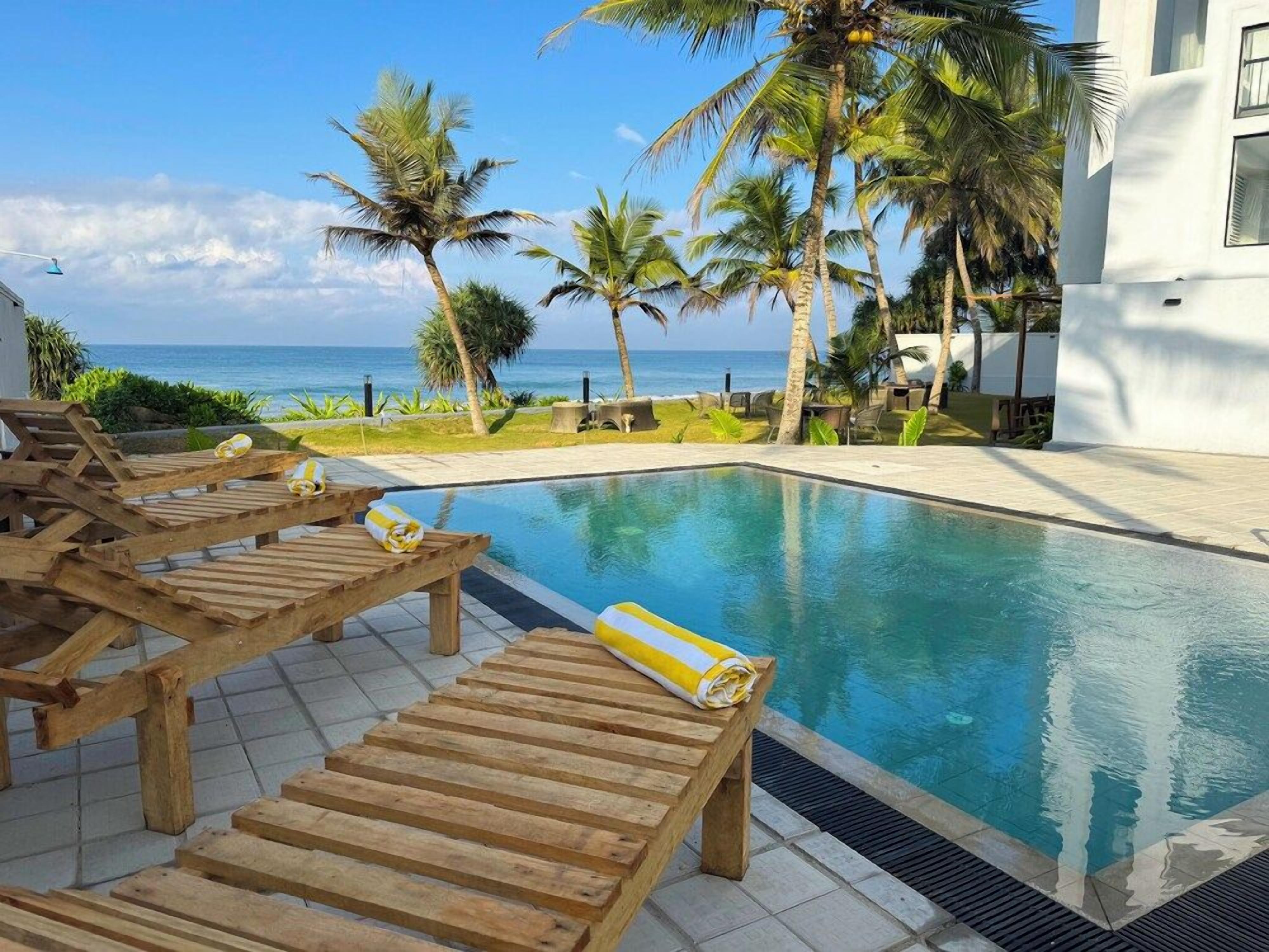A pool area with wooden loungers and a view of the ocean.