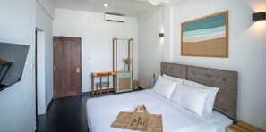 A hotel room with a bed, a desk, a chair, a TV, and a painting on the wall.