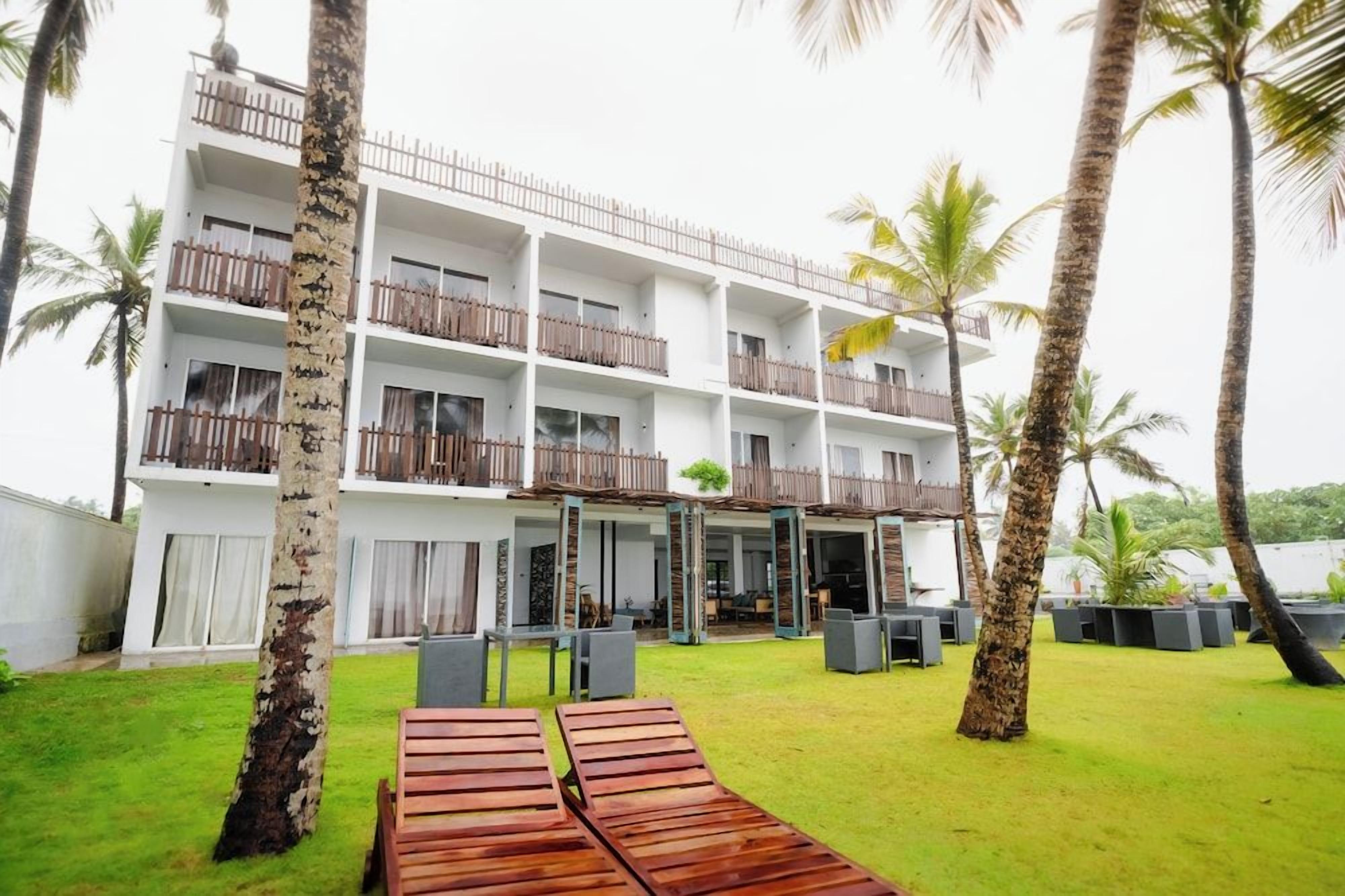 A multi-story hotel with balconies, outdoor seating, and palm trees.